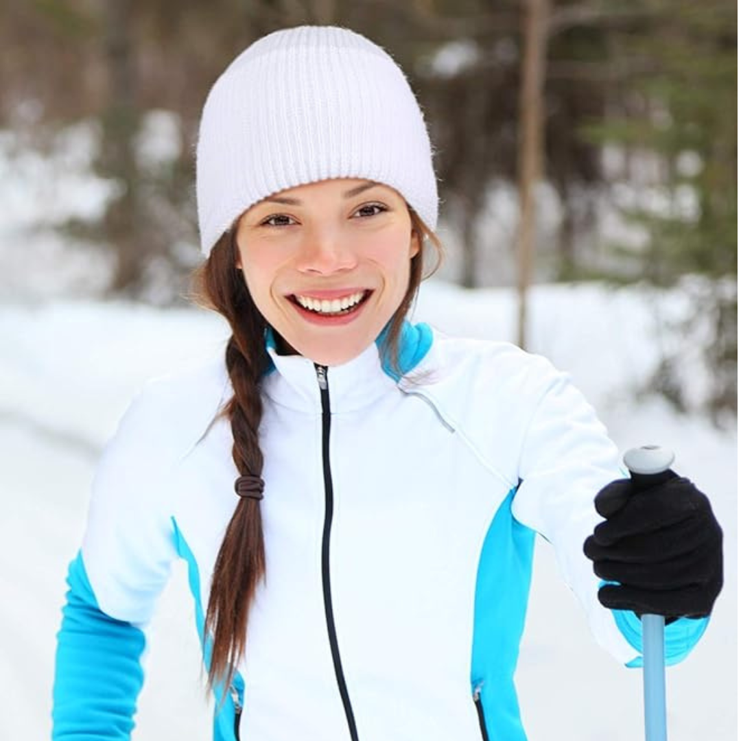 Woman in winter clothing with a ski pole, standing in a snowy forest.